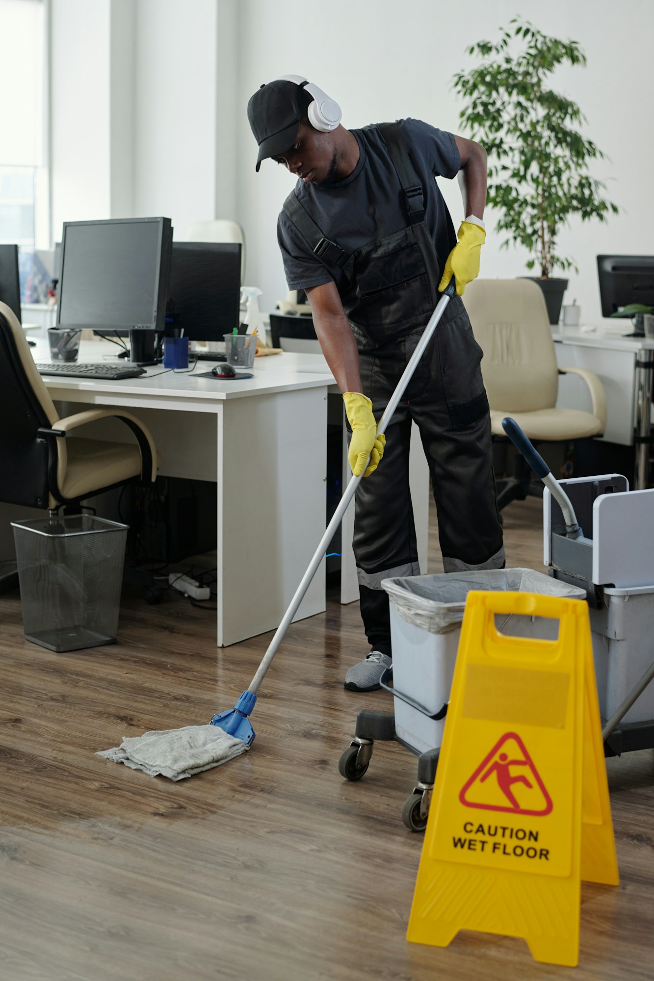 Male janitor in headphones bending forwards while washing floor in office