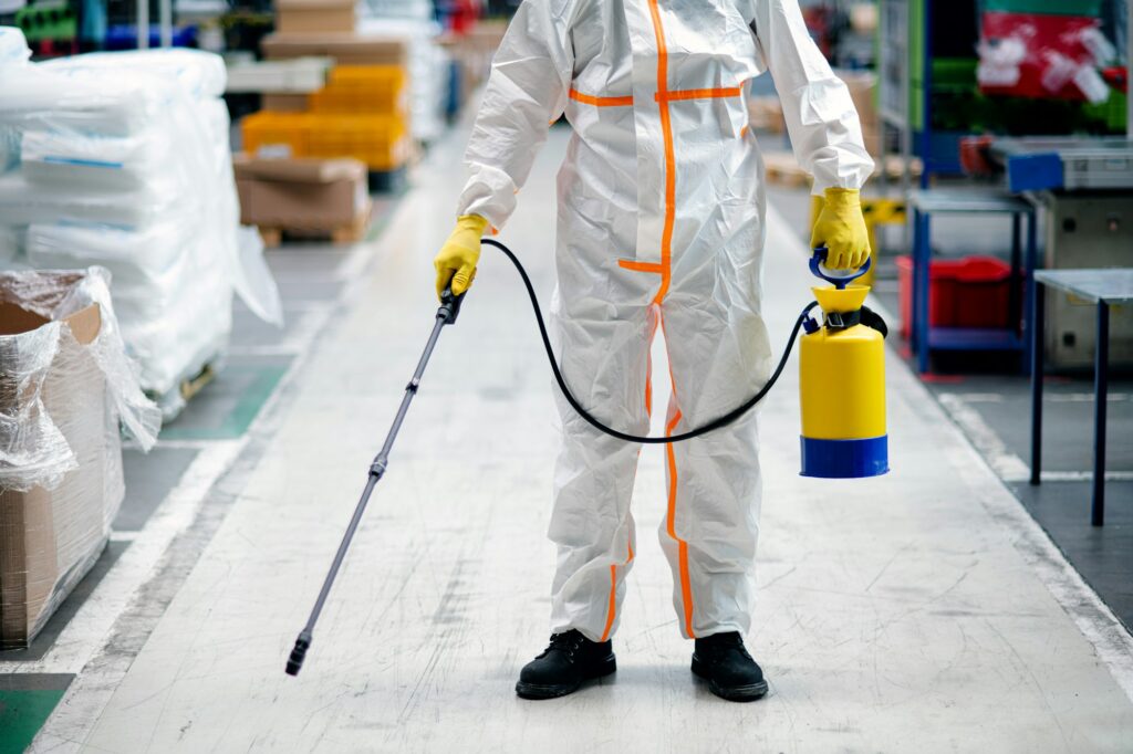 Man worker with protective mask and suit disinfecting industrial factory with spray gun